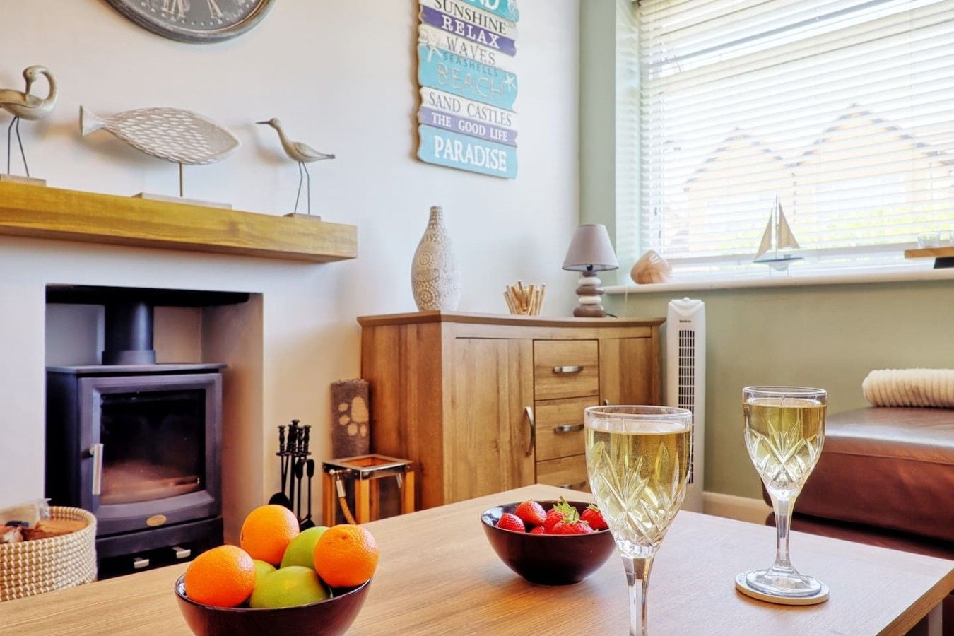 Una sala de estar acogedora con chimenea, muebles de madera, una mesa de comedor con frutas y vasos, y decoración en las paredes.