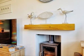 A living room with a fireplace, a television, and decorative items on a shelf. - Luxury Estuary view 1BR in Prime Location (Essex)