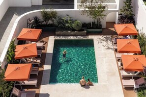 Piscina no terraço com água cristalina, rodeada por espreguiçadeiras e guarda-sóis laranja.