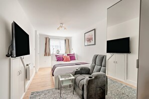 A modern bedroom with a bed, a grey armchair, a small table, and two TVs mounted on the walls. - Host Stay Poplar Apartment (Rochester)