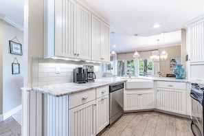 A modern kitchen with white cabinetry, a built-in dishwasher, a coffee maker, and a stove. - Ground-Floor Golf Course Retreat (Miramar Beach)