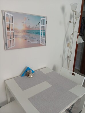 Un comedor con una mesa, sillas, un cuadro de una escena de playa y una planta decorativa.