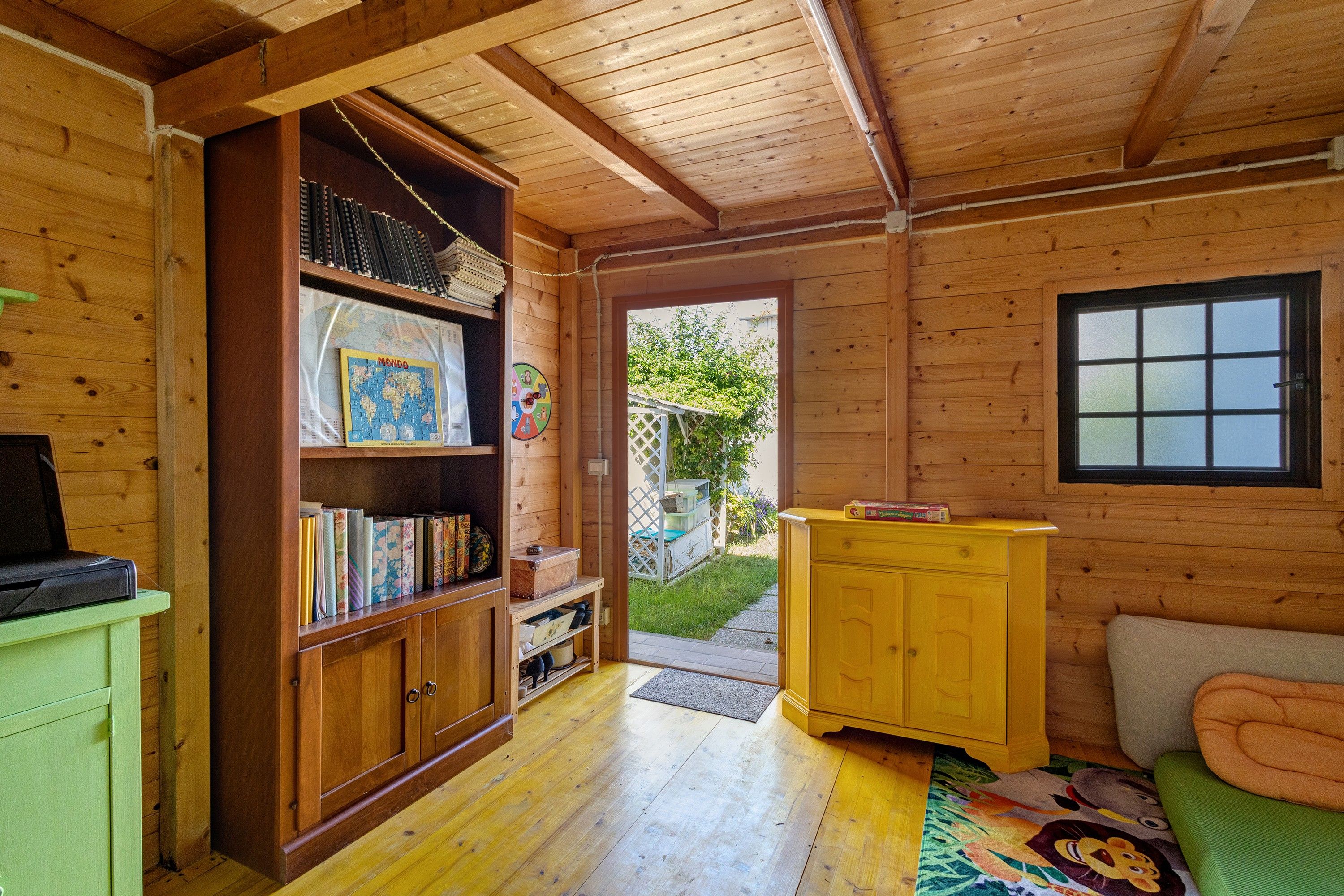 A wooden interior with a bookshelf, a small table, and a window.