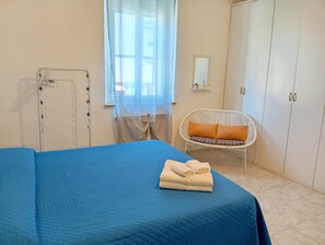 Un dormitorio con cama, una silla, un armario y una ventana.