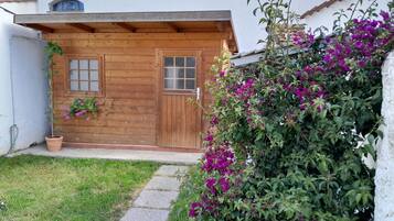 Ett trähus med en liten veranda, en krukväxt och en blommande buske.