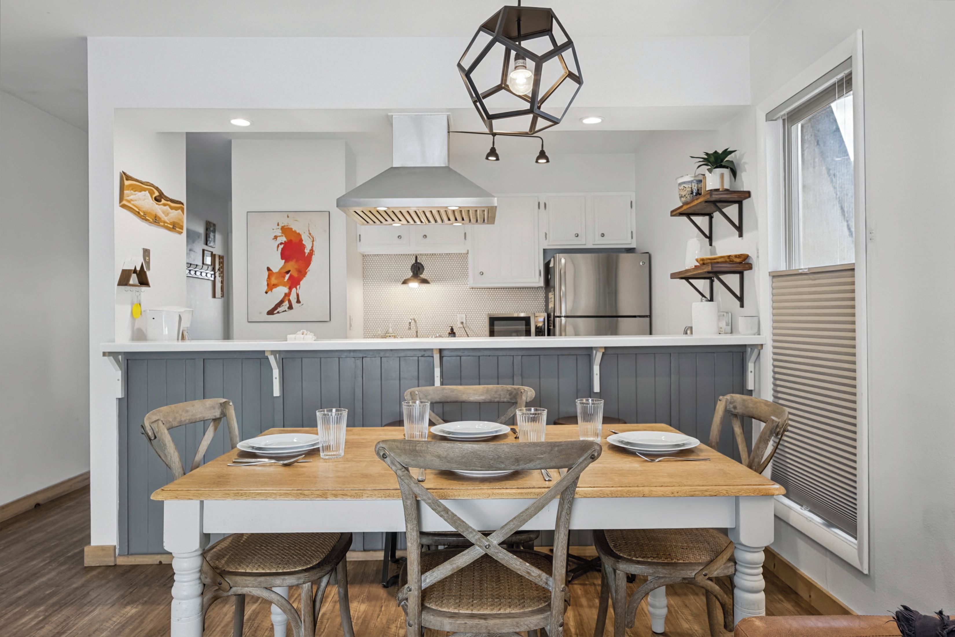 A modern kitchen with a central island, white cabinetry, and a dining area with a wooden table and chairs.