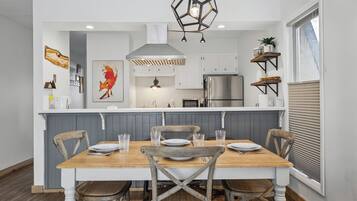 A modern kitchen with a central island, white cabinetry, and a dining area with a wooden table and chairs.