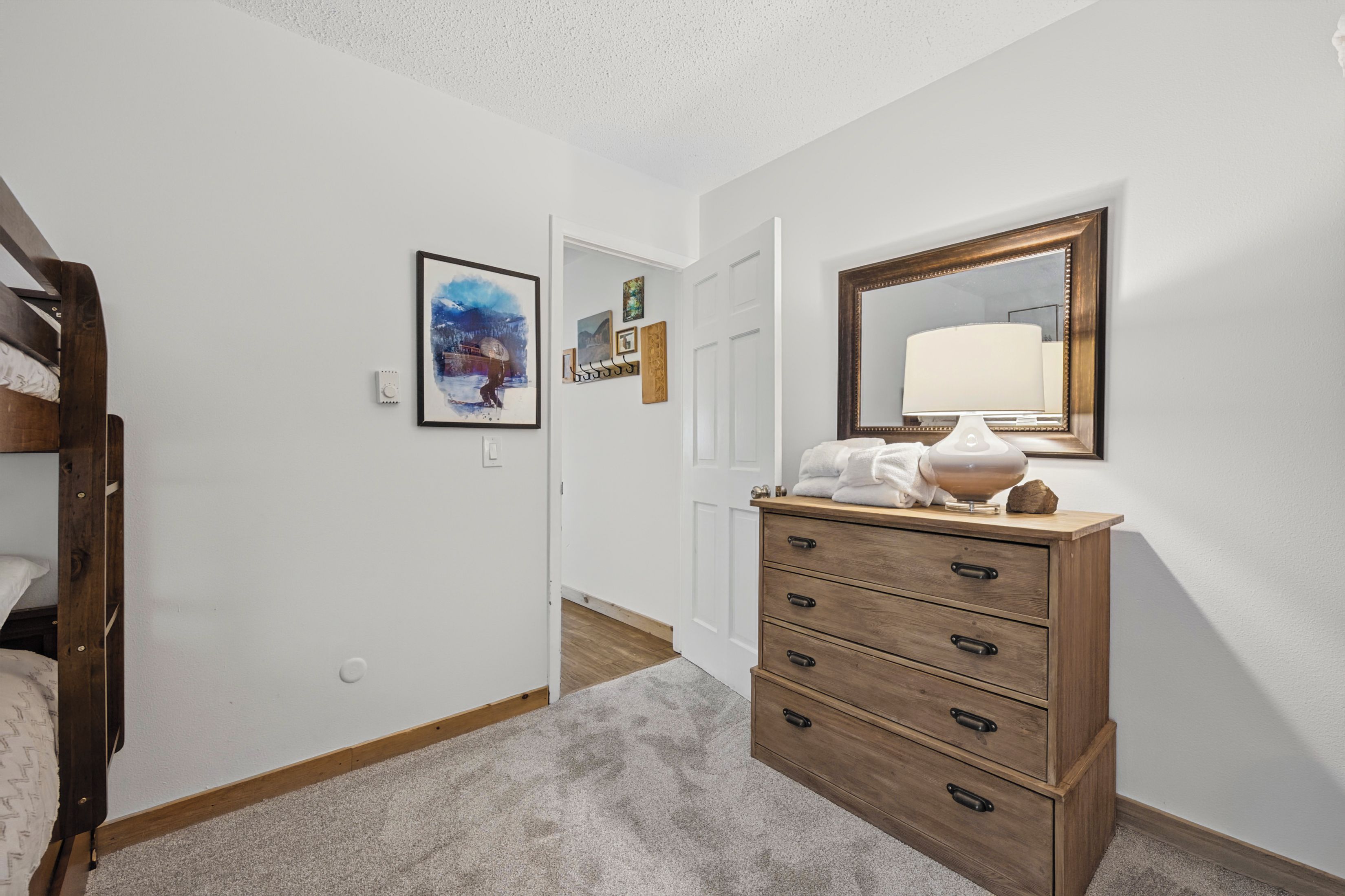 A hallway with a wooden dresser, a mirror, and a framed picture on the wall.