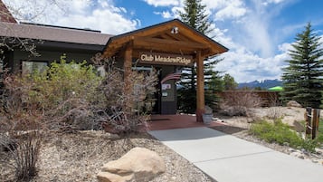 A lodge named Club Meadow Ridge with a wooden entrance pavilion, a flag, and a view of mountains in the background.