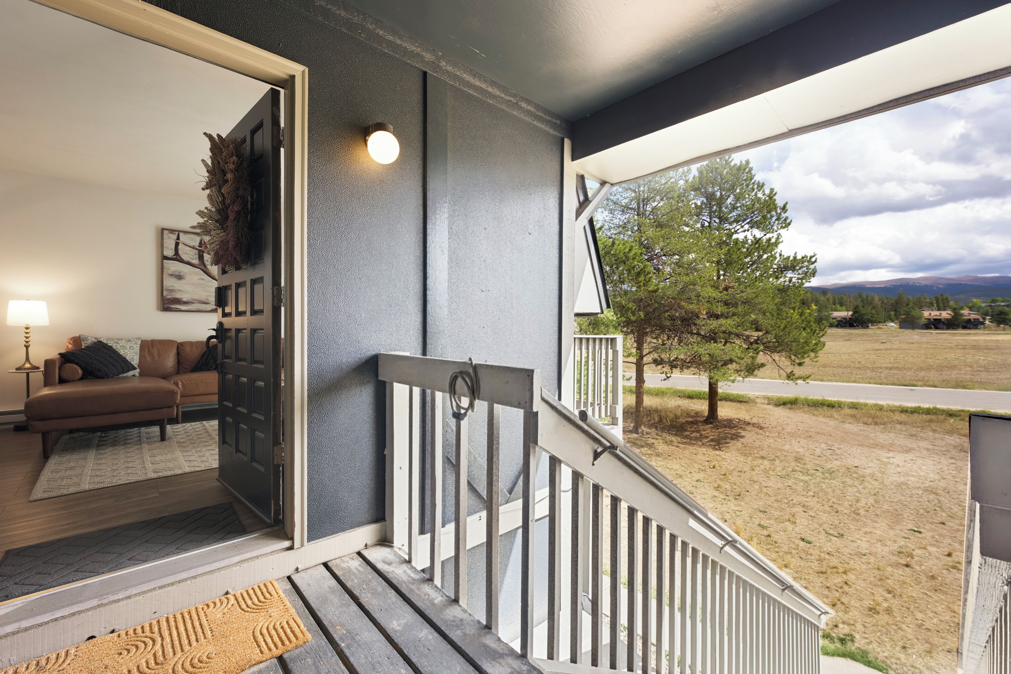 A residential entryway with a staircase leading to a porch, a seating area with a sofa and cushions, and a view of a tree and landscape.
