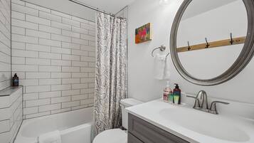 A bathroom with a white bathtub, a toilet, a vanity with a mirror, and a shower curtain.