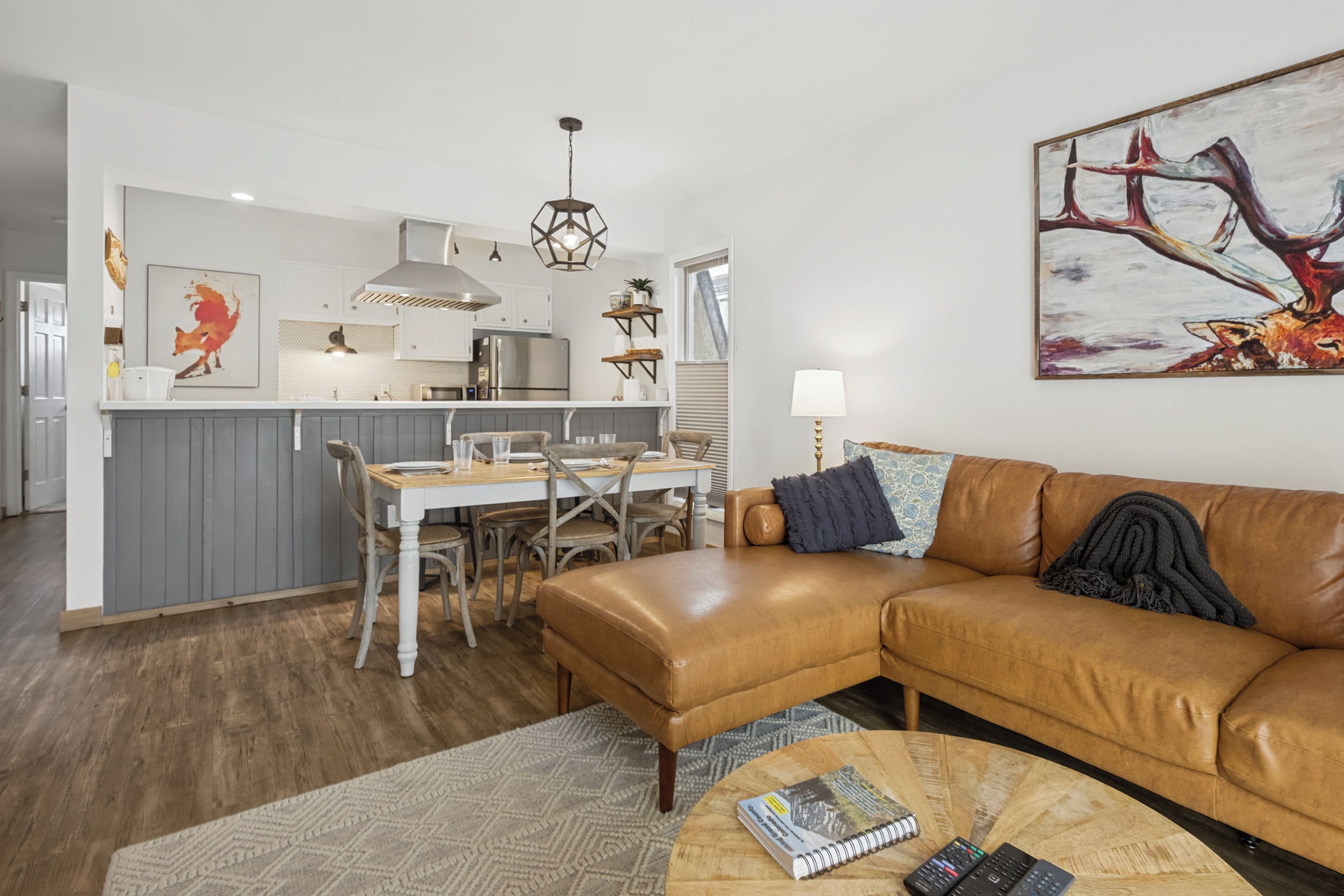 Ein modernes Wohnzimmer mit Ledersofa, ein Essbereich mit Holztisch und Stühlen sowie eine Küche mit Edelstahlgeräten.