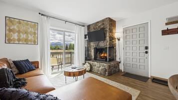 Unwind in your inviting living room with a cozy stone fireplace and mountain views beyond the balcony. Warm leather seating and natural light create the perfect space for relaxation after your alpine adventures.