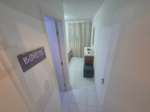 A hallway leading to a bedroom with a bed, a nightstand, and a window with curtains. - Porto Paradise, 300 meters from the sea. (Ipojuca)