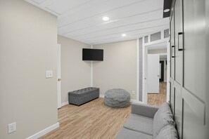 Ett modernt vardagsrum med en grå soffa, en grå pall och en platt-TV som är monterad på väggen.