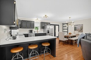 A modern kitchen with a central island, bar stools, and a dining area with a table and chairs. - Asheville Mountain Retreat w Hot Tub & Game Room! (Asheville)