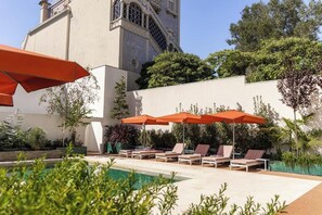 A poolside area with lounge chairs and umbrellas, a building with a tiled facade, and greenery. - Vila Catarina Luxury Apartments: Standard Apartment with Balcony and Pool View (Porto)