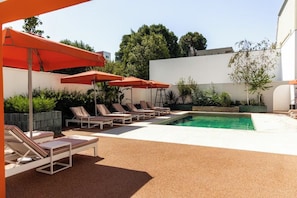 A poolside area with sun loungers and umbrellas, surrounded by greenery and a white building. - Vila Catarina Luxury Apartments: Standard Apartment with Balcony and Pool View (Porto)