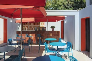 An outdoor patio with round tables and chairs, red umbrellas, and a bar area with wooden furniture. - Vila Catarina Luxury Apartments: Superior Apartment with Private Terrace (Porto)