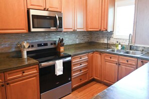 Una cocina con armarios de madera, un microondas de acero inoxidable, una estufa y un lavaplatos.
