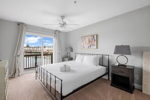 Una habitación de hotel con cama, mesitas de noche, ventilador de techo, ventana con cortinas y vistas a edificios.