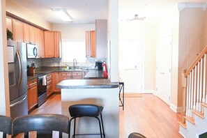 A kitchen with wooden cabinets, a stainless steel refrigerator, and a central island with bar stools. - 2 Lowcountry Lakehouse: Child & Pet Friendly! (North Charleston)