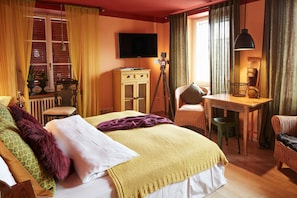Ett hotellrum med en säng, ett skrivbord, en stol, en tv och ett fönster med gardiner.