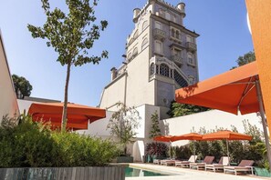 A pool area with lounge chairs and umbrellas, a building with a tower, and greenery. - Vila Catarina Luxury Apartments: Superior Apartment with Balcony and Pool View (Porto)