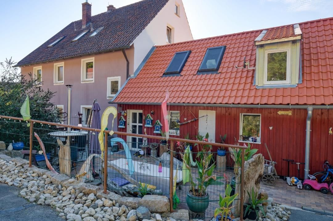 Una propiedad residencial con una casa de techo rojo, un jardín cercado y una variedad de plantas en macetas.