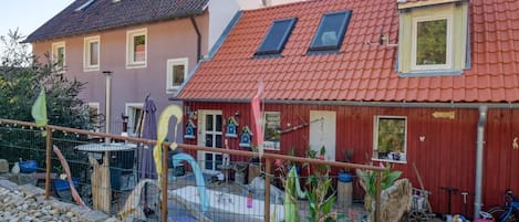 A residential property with a red-roofed house, a fenced garden area, and a variety of potted plants.