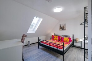 Une chambre avec un puits de lumière, un lit avec une literie aux couleurs vives, une petite table de chevet et un radiateur.