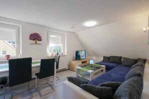 Un salon moderne avec un canapé, des fauteuils, un téléviseur et une petite table.