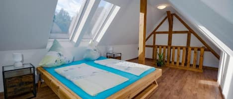 A bedroom with a sloped ceiling, wooden beams, a bed with blue bedding, and skylights.