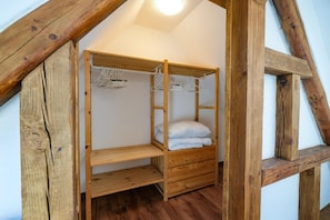 A wooden bunk bed with a shelf below and a hanging rack above, in a room with exposed wooden beams and a sloped ceiling. - Vacation Rental 2 with a Forest View Near Bayreuth (Mistelgau)