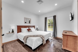 A bedroom with a bed, bedside tables, a nightstand, a dresser, a window with curtains, and a wall-mounted TV. - Branson Lodge, Hot Tub, 6 King Rooms, 2 Bunk Rooms (Branson)