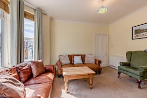 A living room with a brown leather sofa, a wooden coffee table, and a green armchair. There is a door and a framed picture on the wall. - Host Stay House On The Hill (Hastings)