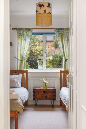 Une chambre avec deux lits, une fenêtre avec des rideaux, un radiateur et une commode en bois.