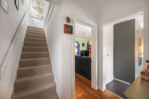 Eine Treppe führt zu einem mehrstöckigen Innenraum mit einer Tür, einem Wandbild und einem kleinen Tisch mit einem dekorativen Gegenstand.