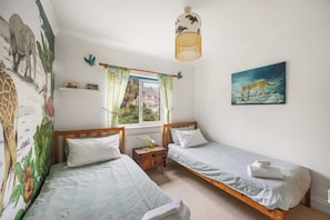 Ein Schlafzimmer mit zwei Einzelbetten, einem Fenster mit Vorhängen, einem Bild an der Wand und einem Wandgemälde.