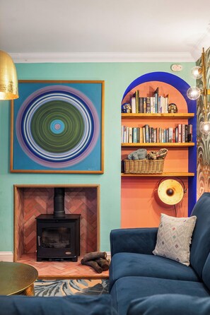 A living room with a blue sofa, a fireplace, a bookshelf, and a large abstract painting. - Colourful Lewes Home | Garden | Free Parking (East Sussex)