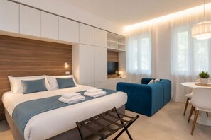 Una habitación de hotel moderna con una cama grande, una zona de estar con un sofá azul, una mesita y un escritorio.