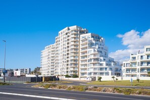 A multi-story hotel with balconies, a parking lot, and a clear sky. - The Bay A801 - Two Bedroom Apartment, Sleeps 4 (Cape Town)