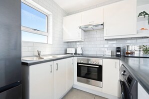 Cocina moderna con muebles blancos, refrigerador de acero inoxidable, horno Bosch y ventana que proporciona luz natural.