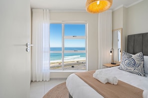 A hotel room with a large window offering a view of the beach and ocean. - The Bay A801 - Two Bedroom Apartment, Sleeps 4 (Cape Town)