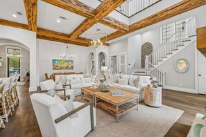 Ein geräumiges Wohnzimmer mit hohen Decken, Holzbalken, weißen Wänden und einer Treppe.