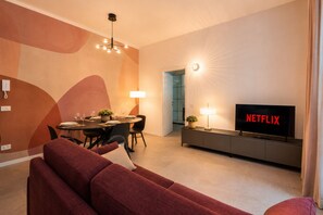 Ein modernes Wohnzimmer mit einer Couch, einem Esstisch und einem Fernseher, der 'NETFLIX' anzeigt.