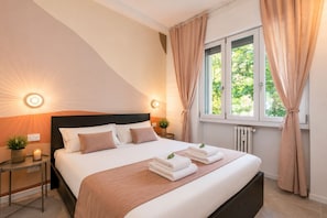 Ein Hotelzimmer mit Bett, Nachttischlampen, einem Fenster mit Vorhängen und einem Heizkörper.