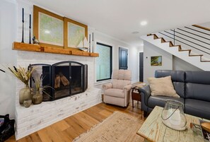 A living room with a fireplace, a sofa, a chair, and a staircase. - Lakefront Family Escape | Dock, Fire Pit & More (Flowery Branch)