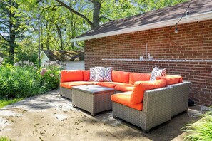 Une terrasse extérieure avec un ensemble de meubles de jardin en osier et une petite table, le tout entouré d’un mur de briques et de verdure.