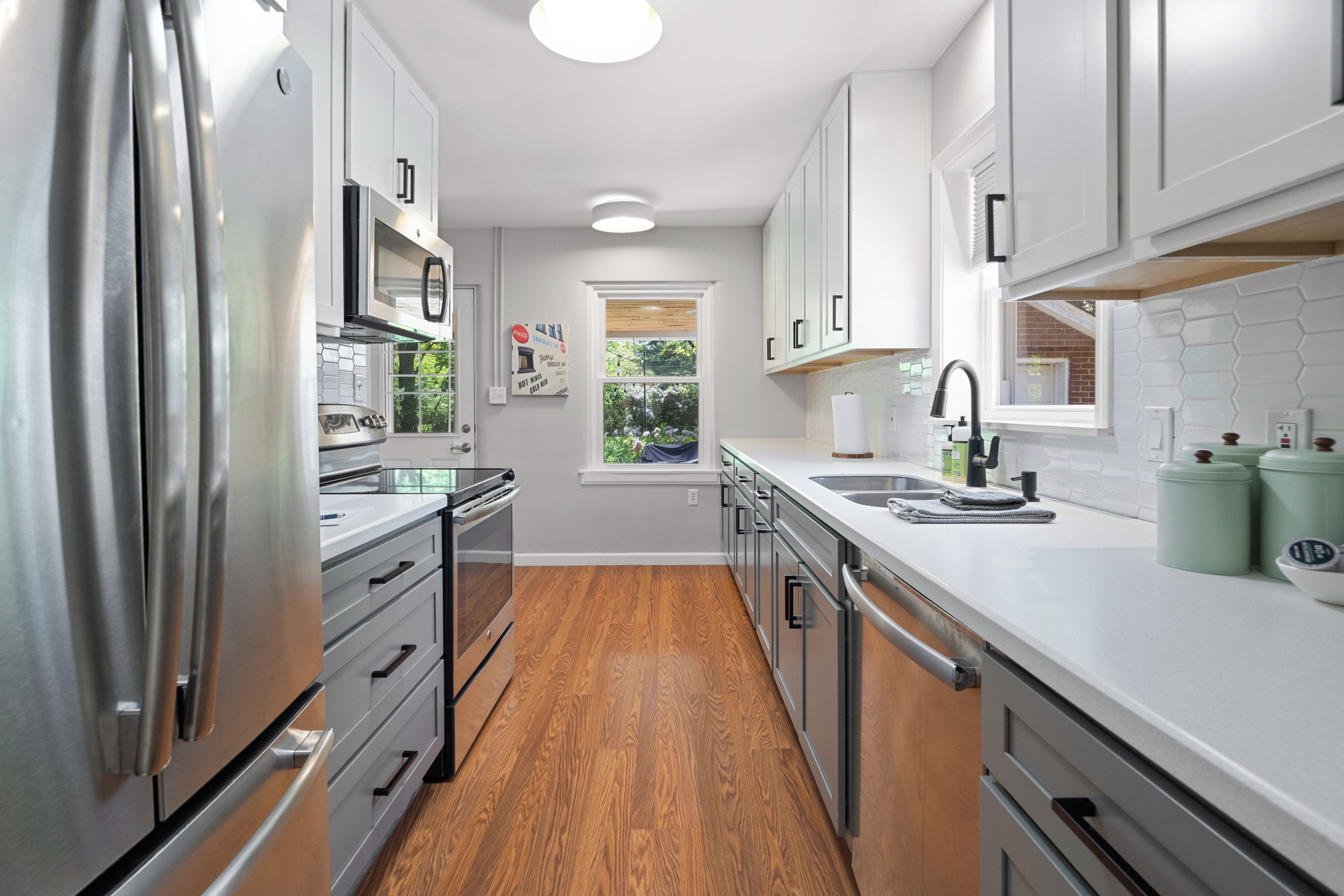 Una cocina moderna con electrodomésticos de acero inoxidable, armarios blancos y piso de madera.